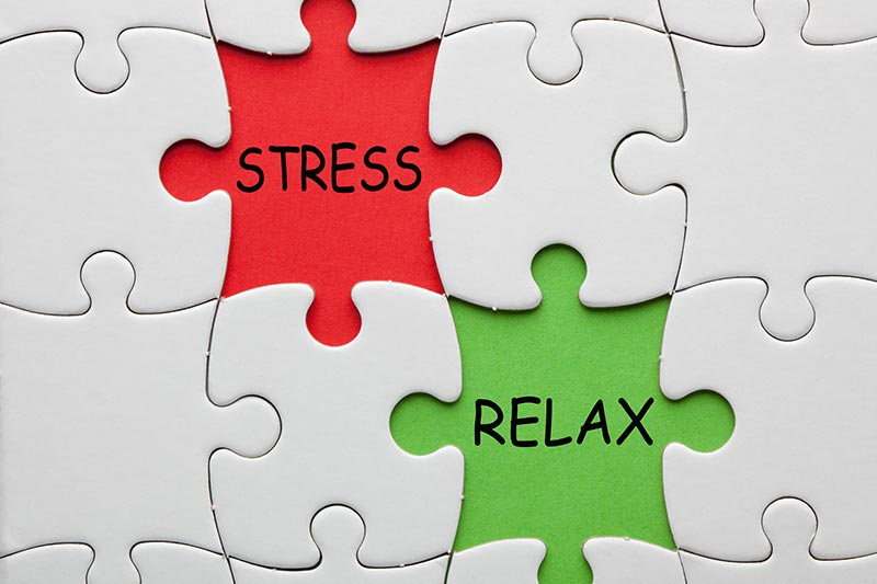 Witte puzzelstukjes met daarin een rood puzzelstukje met de woorden stress en een groen puzzelstukje met de woorden relax.